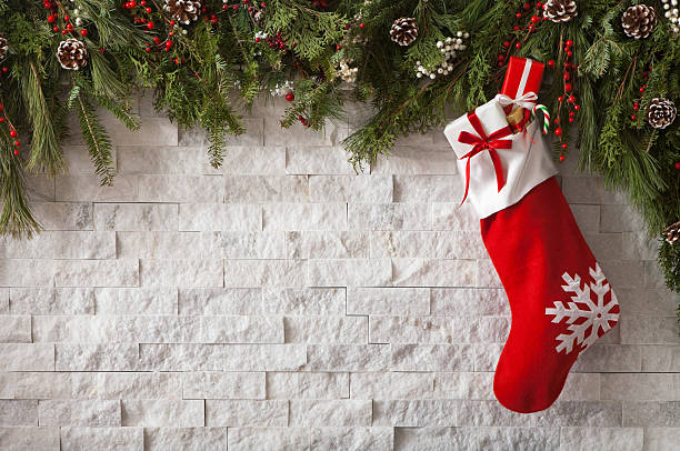 Christmas Stocking with gifts and bow hung on a fireplace with evergreen garland.